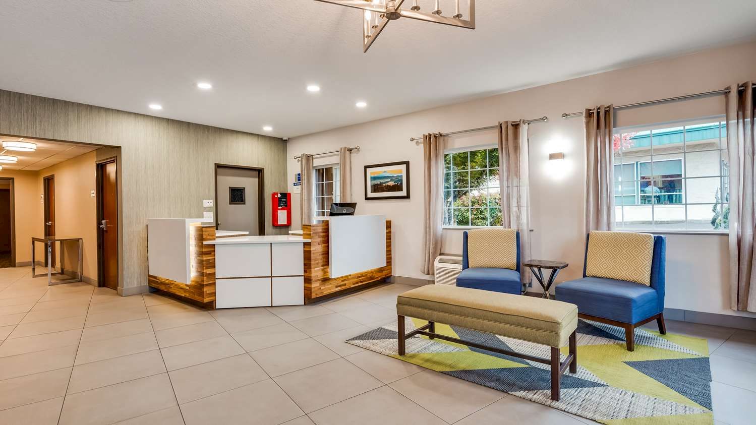 A modern lobby featuring a reception desk, seating area with chairs and bench, wall art, windows, and minimalistic decor.