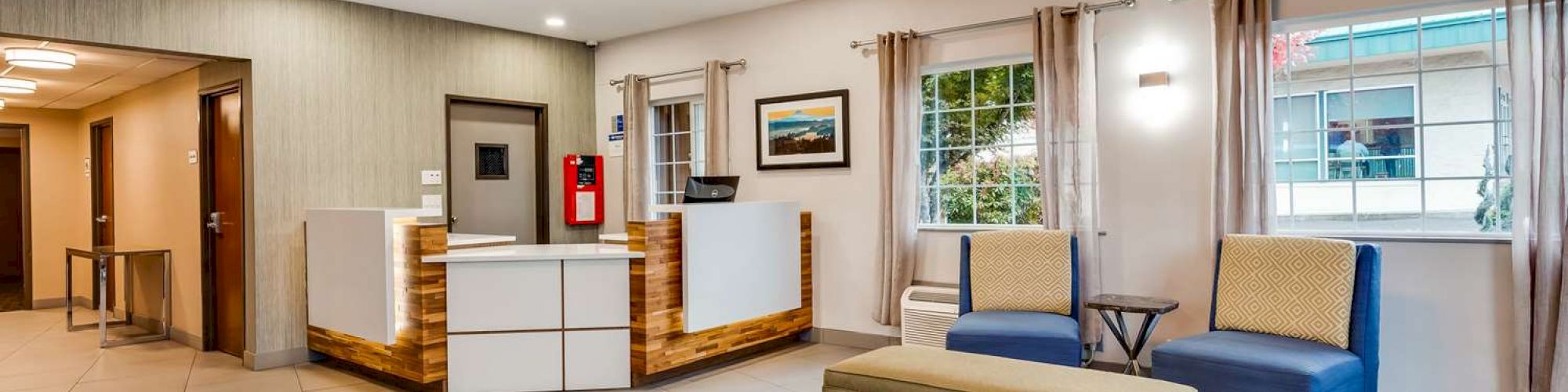 A modern lobby featuring a reception desk, seating area with chairs and bench, wall art, windows, and minimalistic decor.