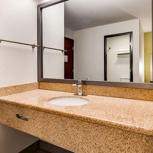 A bathroom with a wide countertop, a sink, a large mirror, a towel rack, and a wall-mounted bottle opener.