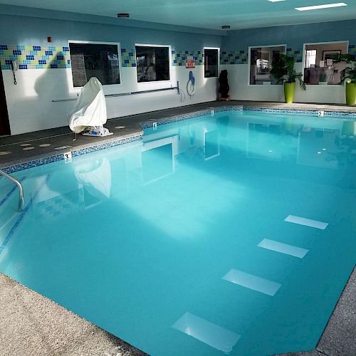 This image shows an indoor swimming pool with clear blue water, a pool lift on the left side, and several windows and doors around the pool area.