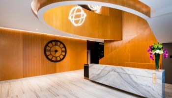This image shows a modern reception area with a marble desk, a large wall clock, wooden paneling, and a spiral architectural feature.