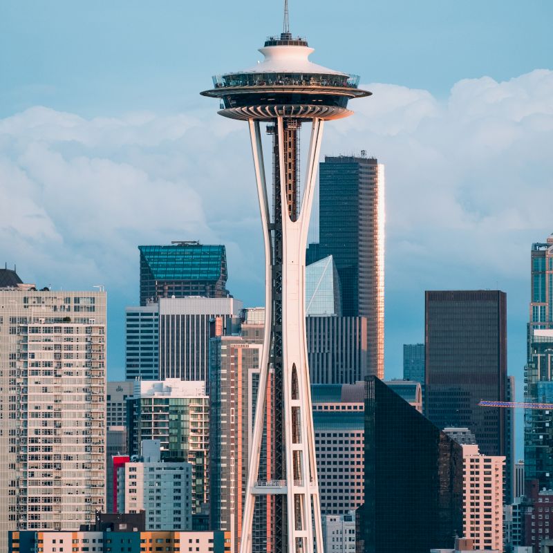 A cityscape featuring a tall, uniquely designed tower with a disc-shaped observation deck, surrounded by modern buildings and skyscrapers.