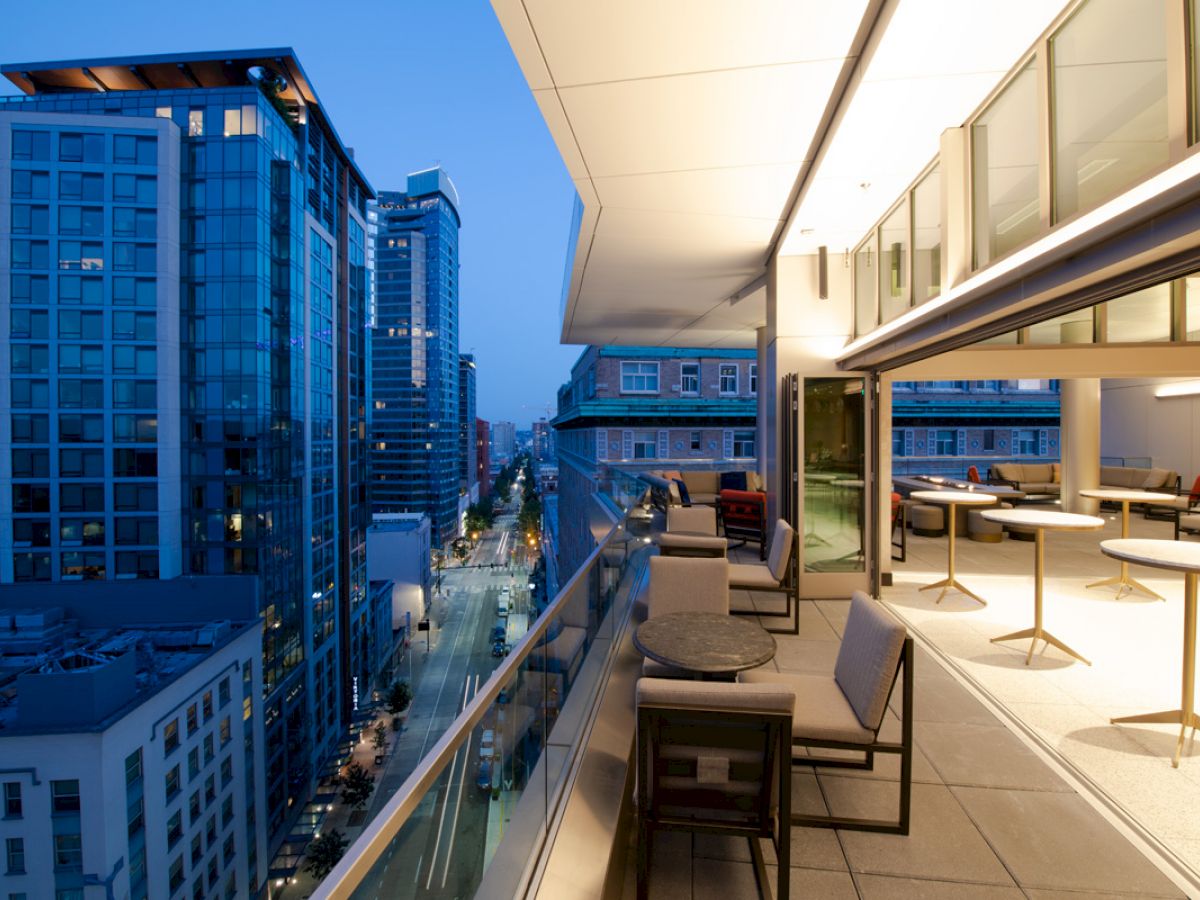 A modern cityscape view with high-rise buildings during dusk, and a sleek balcony with seating arrangements overlooking the street below.