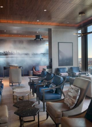 A modern lounge area with numerous chairs, large windows with a waterfront view, and a mural of a city skyline on the wall.