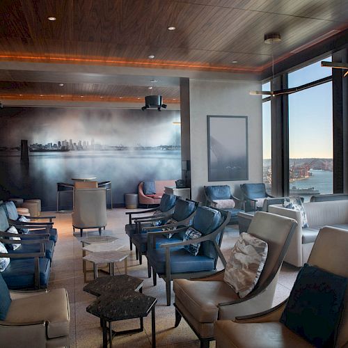A modern lounge area with comfortable seating, a mural on the wall, large windows offering a view of a Ferris wheel and waterfront scenery.