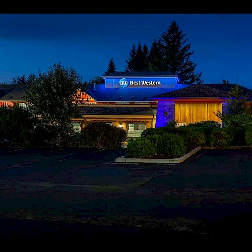 The image shows a Best Western hotel at night, with illuminated signs and a dark parking lot surrounded by trees and landscaping.