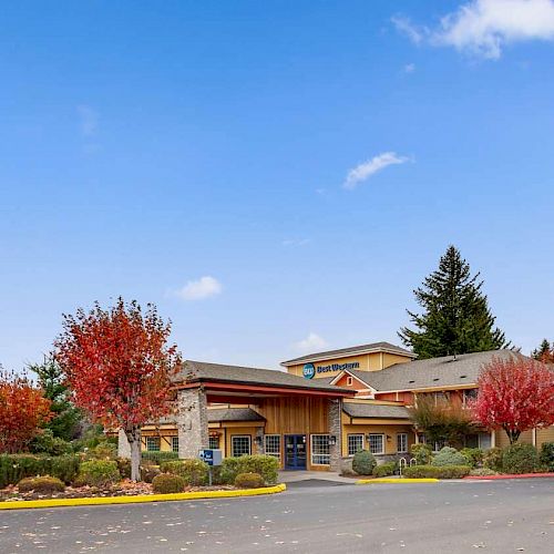 The image shows a building surrounded by colorful trees and a clear blue sky with scattered clouds. The sign reads 