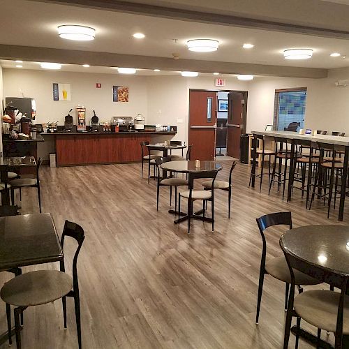 The image shows a modern dining area with several tables and chairs, a coffee station, and a clean, well-lit atmosphere ending the sentence.