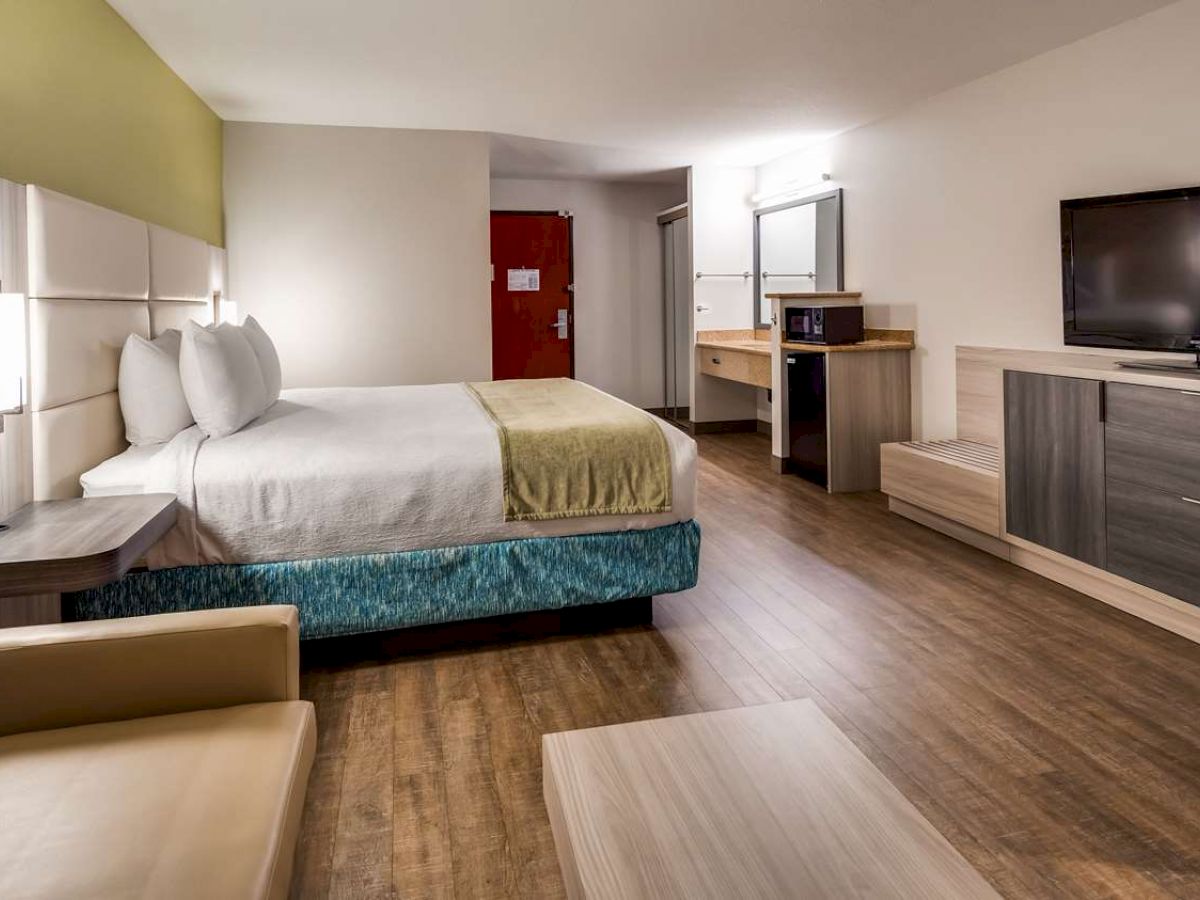 A modern hotel room with a bed, a sofa, a TV, a wooden floor, and a desk with a mirror and chair.